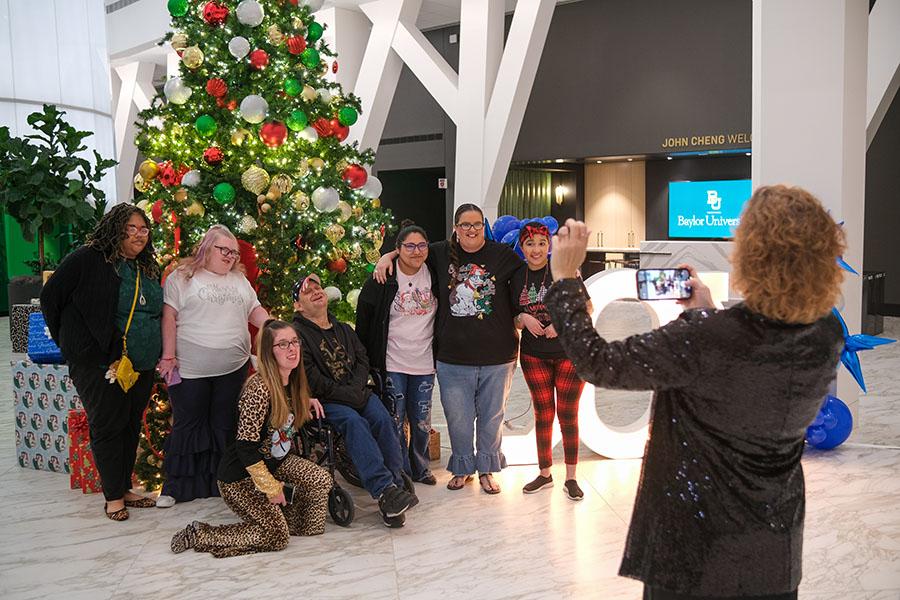 A Special Starry Night attendees taking a picture in front of the tall, green Christmas tree with red, white and gold ornaments on it.